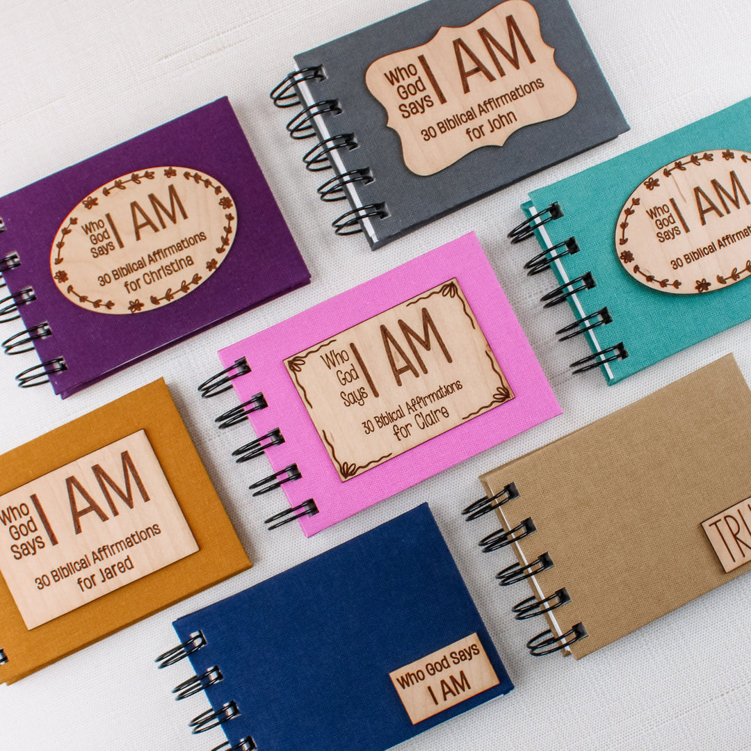 Colorful bookcloth Christian affirmation books with wooden plaques reading “Who God Says I AM,” including personalized options.