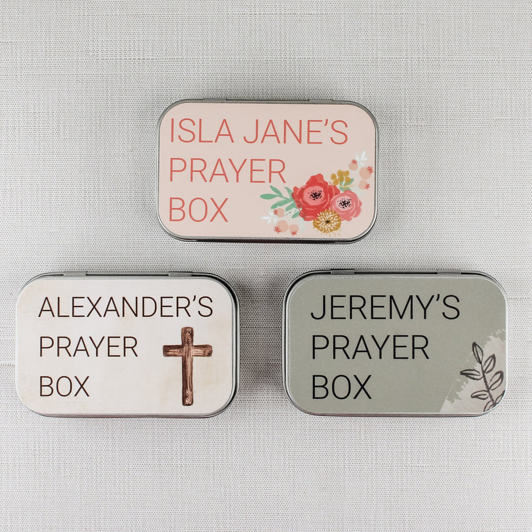 Three personalized metal prayer boxes with floral, cross and leafy designs in pink, cream and sage green.