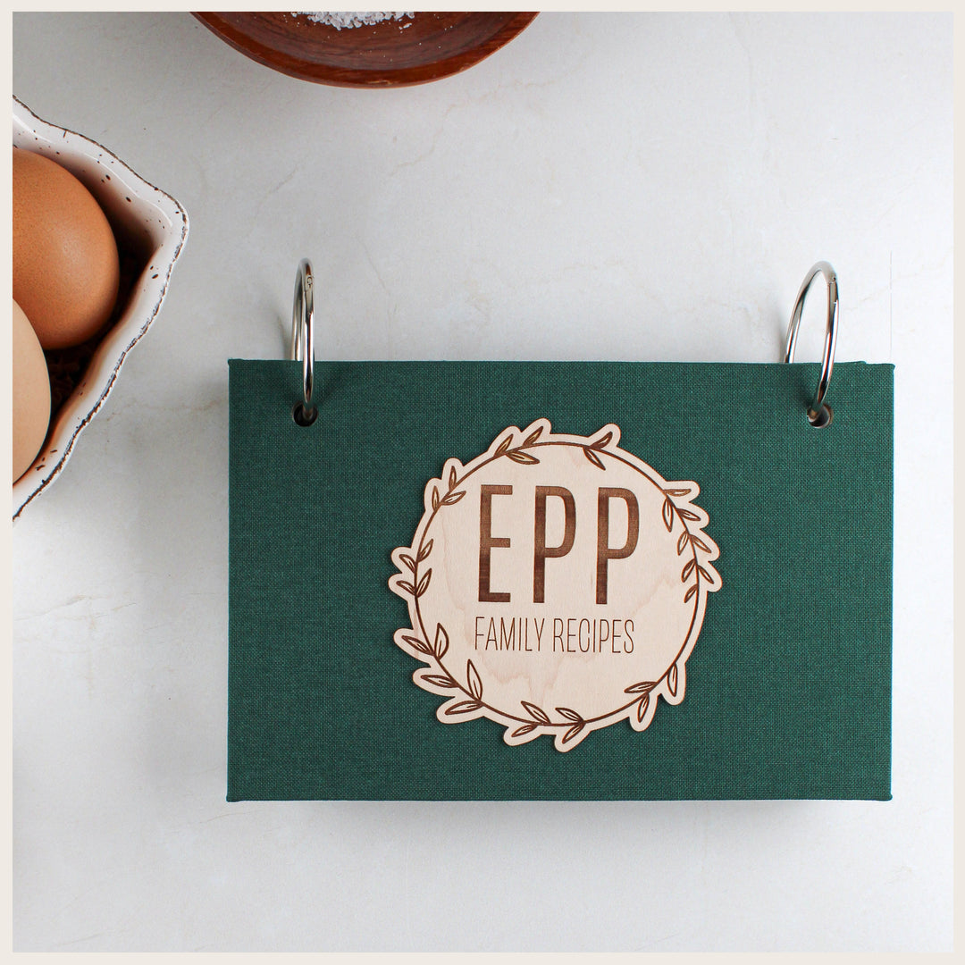 Forest book cloth recipe binder with silver rings and a maple veneer wreath engraved with a family name.