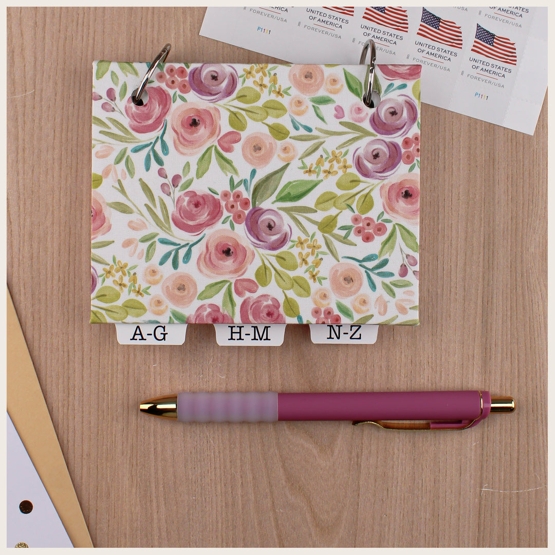 Pastel Floral fabric address book with a blank cover and alphabetical tabs, shown beside postage stamps and a pink pen.