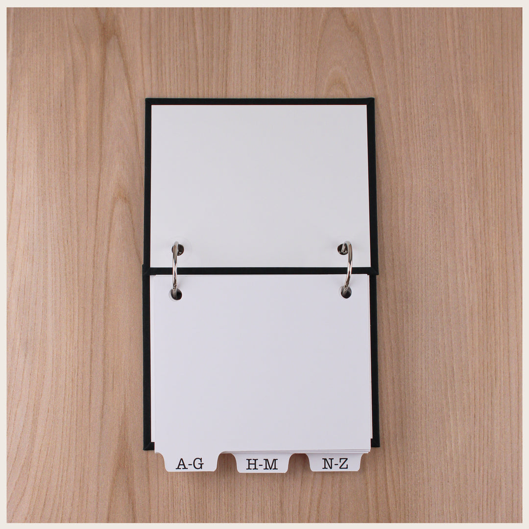 Open password book showing white inside covers, two metal book rings, and alphabetical divider tabs.
