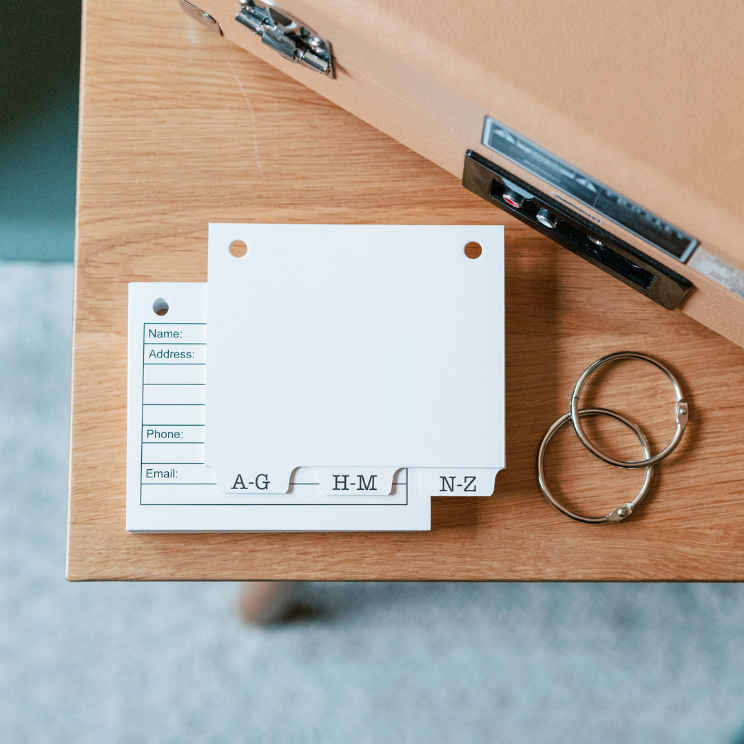refillable address book accessories on a wooden surface. 3 alpha tabs, two 1.5 inch book rings and 50 blank address book cards to refill our address book.