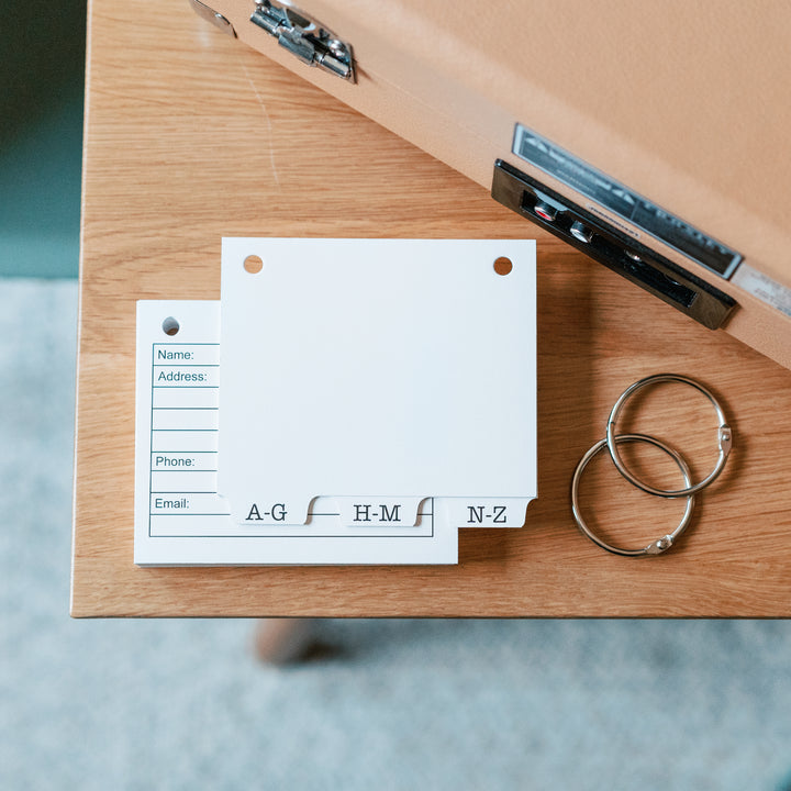 refillable address book accessories on a wooden surface. 3 alpha tabs, two 1.5 inch book rings and 50 blank address book cards to refill our address book.