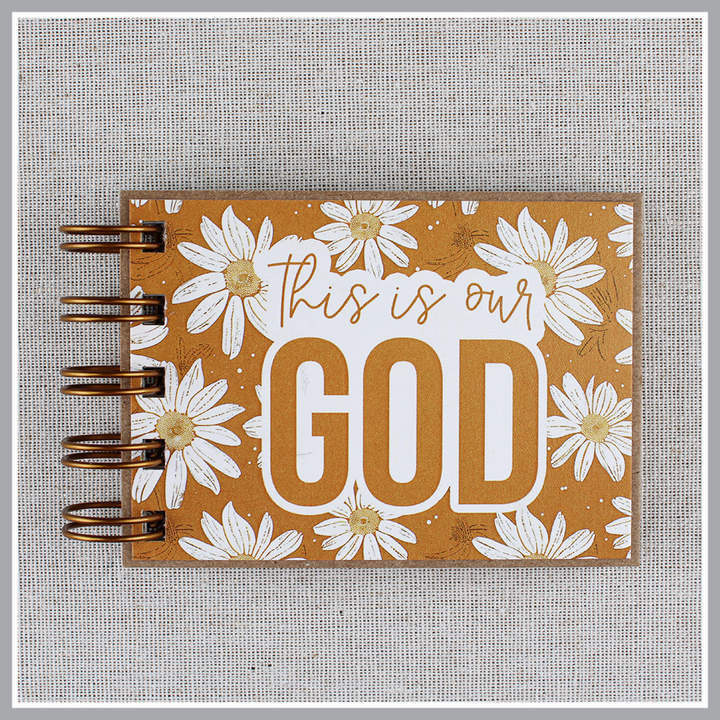 Front cover close up of small spiral bound attributes of God book in Daisy style with yellow background and ivory flowers. Front cover says "this is our GOD".