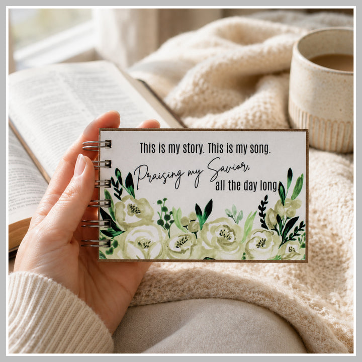 Botanical Christian prayer journal held in hand beside a Bible and coffee.
