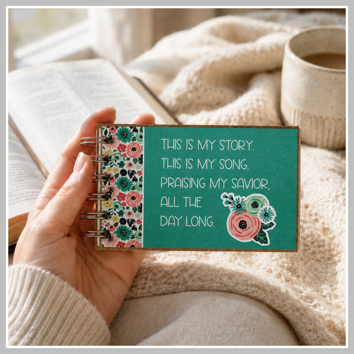 Teal Christian prayer journal held in hand beside a Bible and coffee.