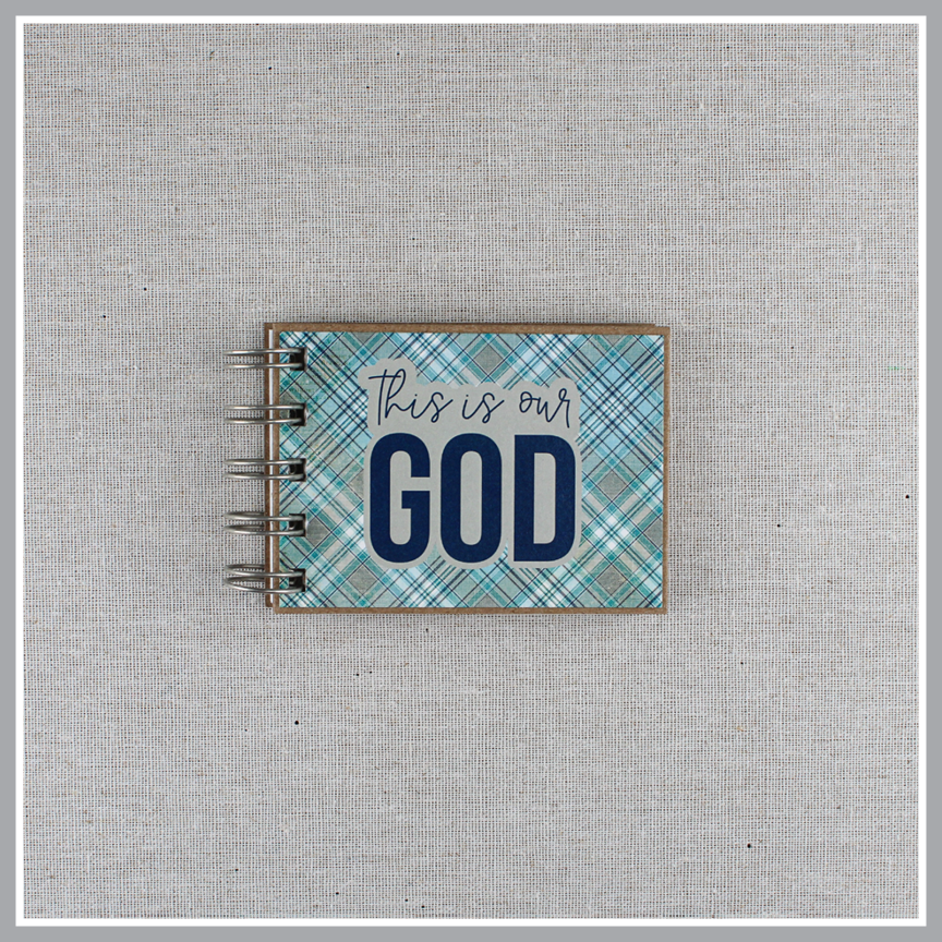 Spiral-bound book with 'This is our God' text on a plaid blue and gray cover.