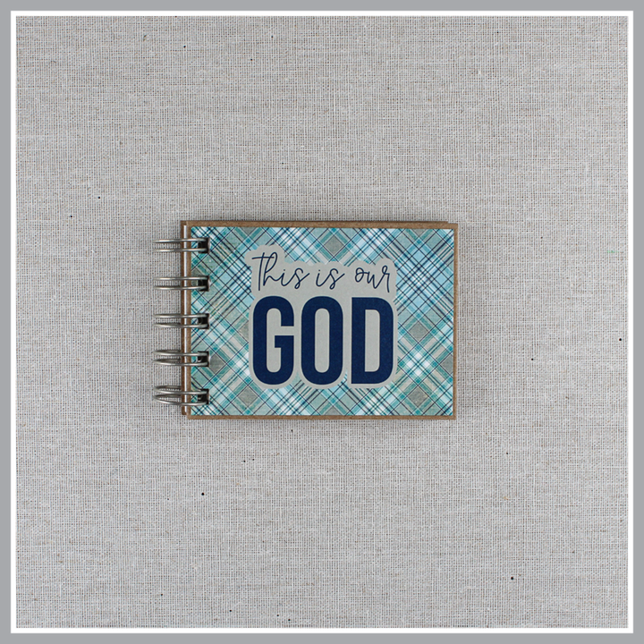 Spiral-bound book with 'This is our God' text on a plaid blue and gray cover.