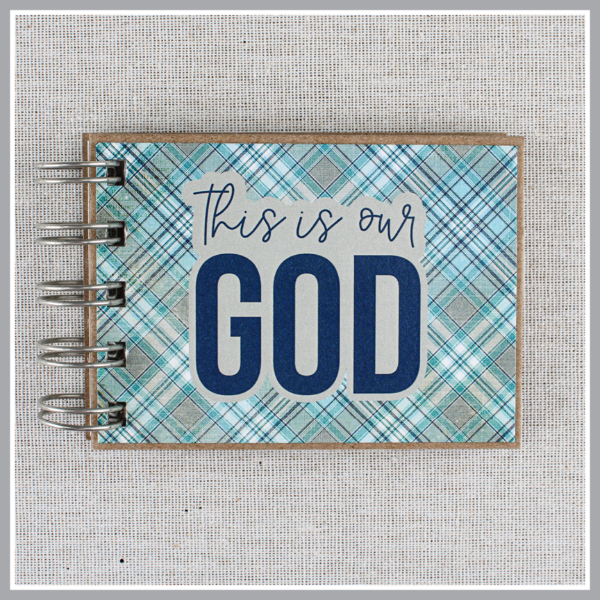 Front cover close up of spiral-bound book with 'This is our God' text on a plaid blue and gray cover.