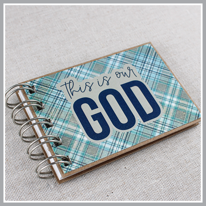 Angled close up of spiral-bound book with 'This is our God' text on a plaid blue and gray cover.
