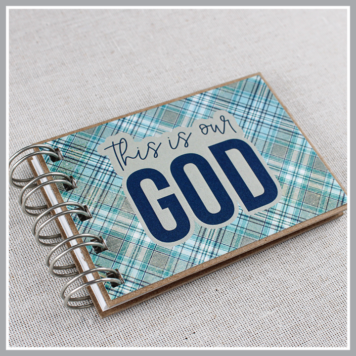 Angled close up of spiral-bound book with 'This is our God' text on a plaid blue and gray cover.