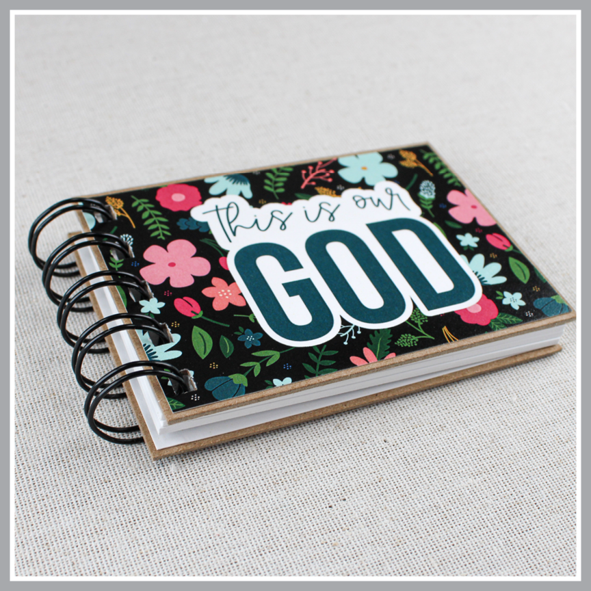Front cover angled close up of God's attributes book with black background and pastel florals. Text says 'this is our GOD'.