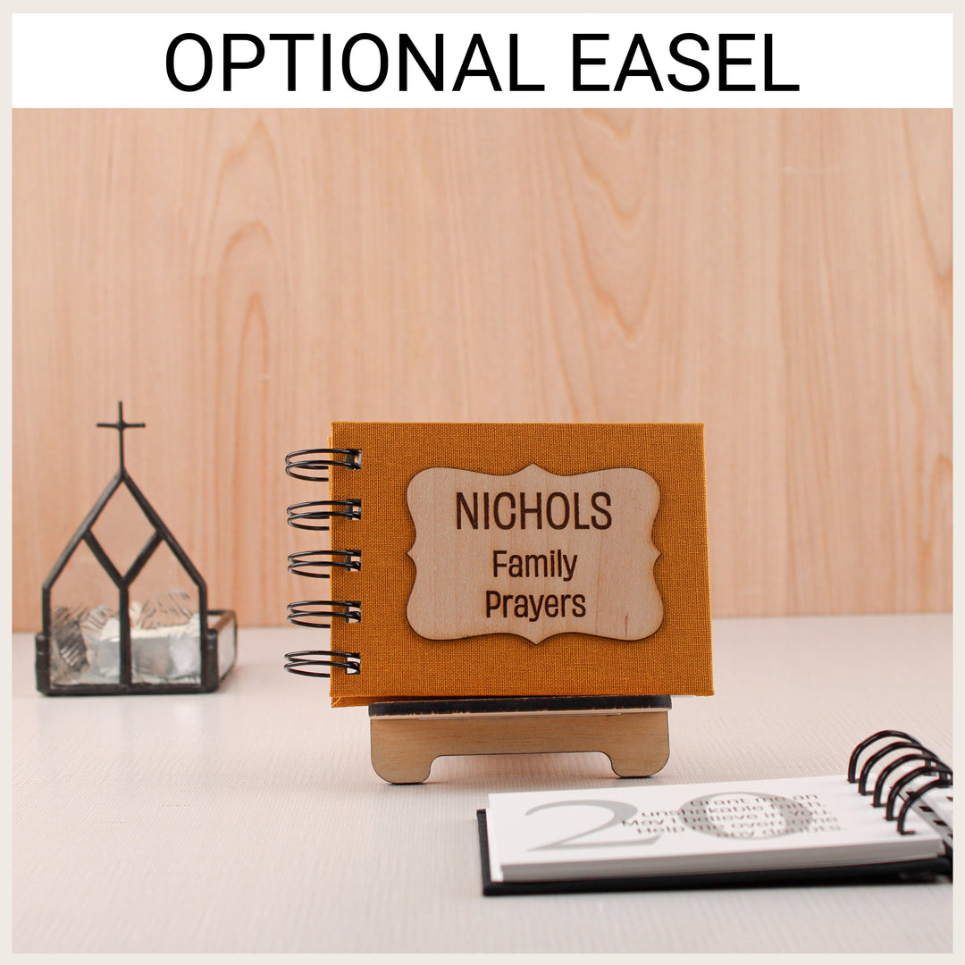Personalized mustard family prayer book displayed on an optional wooden easel, with an open prayer book in the foreground.