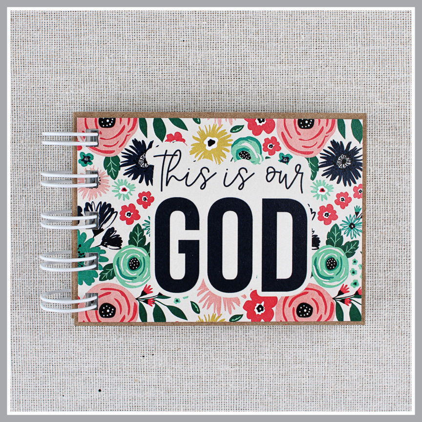 Close up of Gods attributes book in bright floral design with 'This is our GOD' text on a textured gray background.