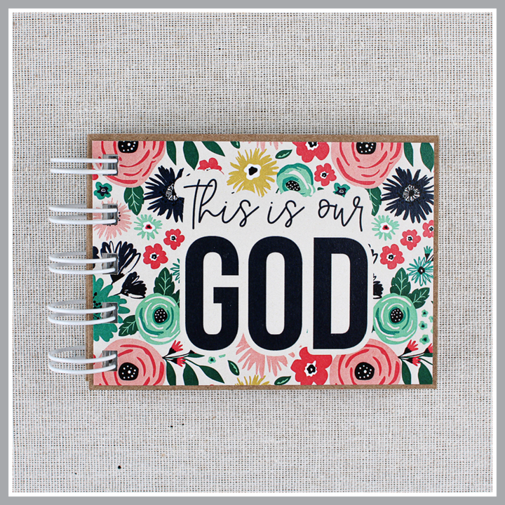Close up of Gods attributes book in bright floral design with 'This is our GOD' text on a textured gray background.