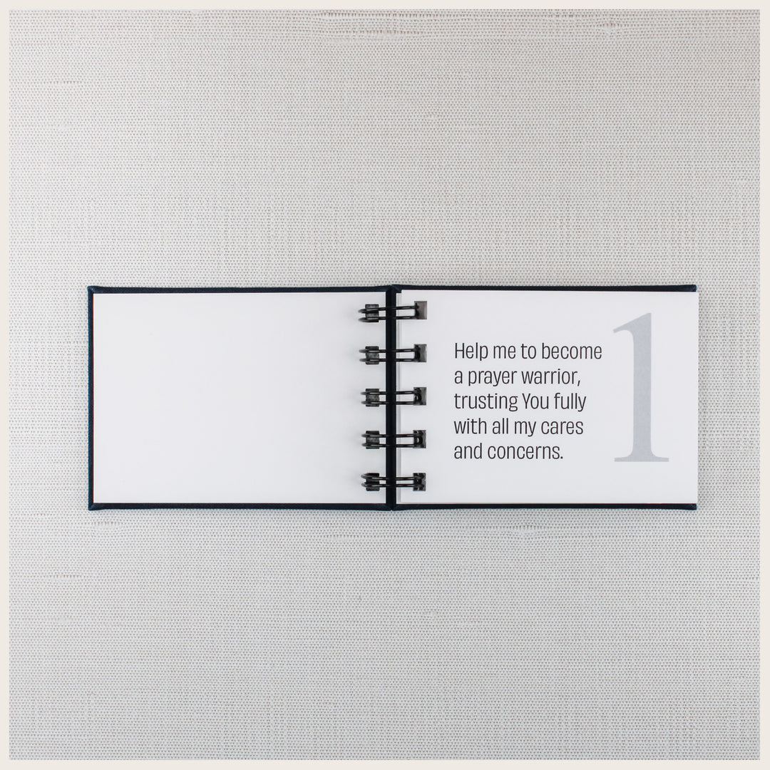 Open navy prayer book showing prayer 1, asking God for help becoming a prayer warrior and trusting Him with personal cares and concerns.