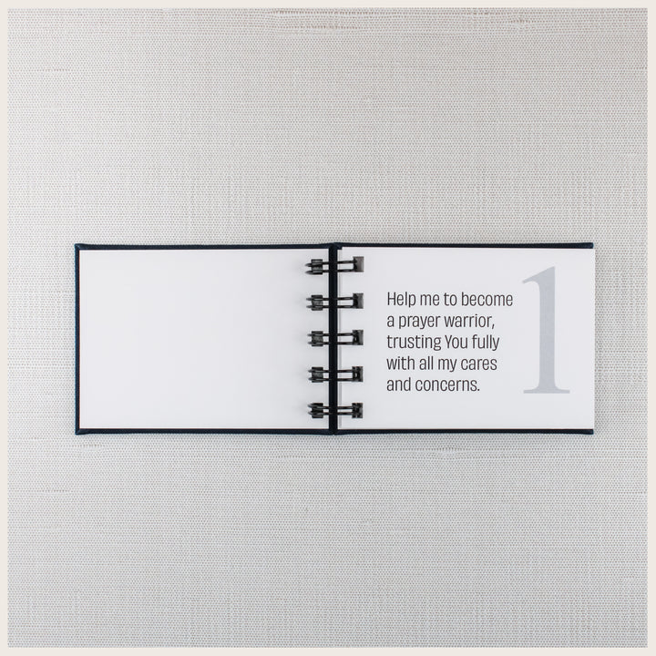 Open navy prayer book showing prayer 1, asking God for help becoming a prayer warrior and trusting Him with personal cares and concerns.