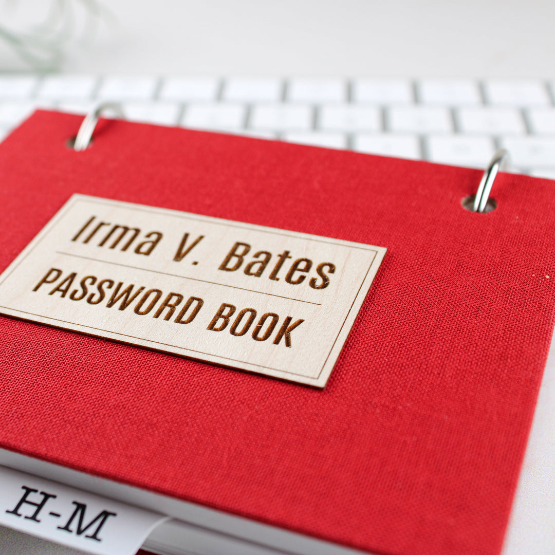 Red bookcloth password book personalized with name on wood veneer.