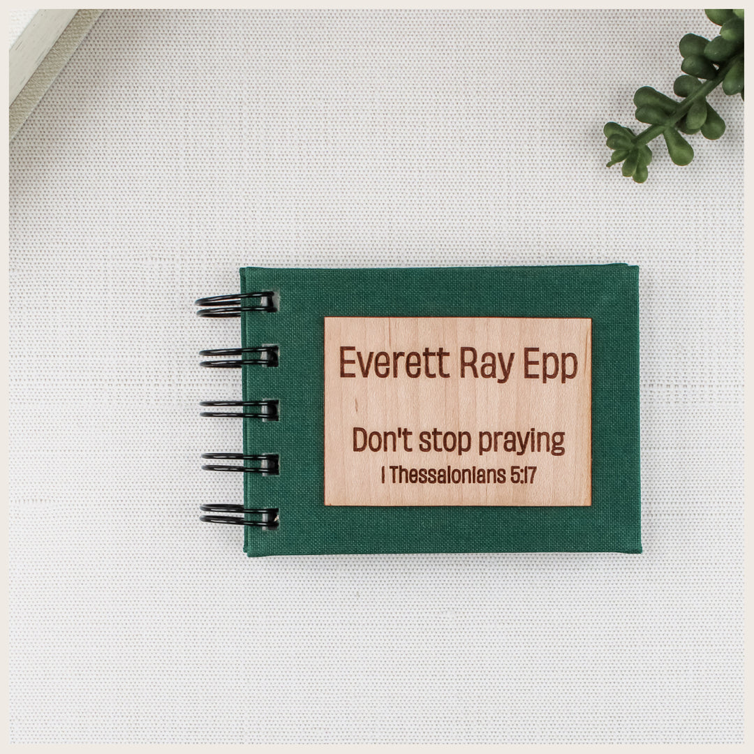 Forest green spiral prayer book with a wood plaque engraved Everett Ray Epp, Don’t stop praying, and 1 Thessalonians 5:17.