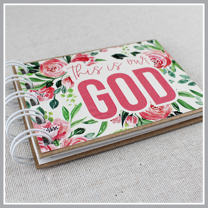 Close up photo at an angle to show details of attributes of God spiral bound book with pink flowers and green leaves. Front cover says "this is our GOD".