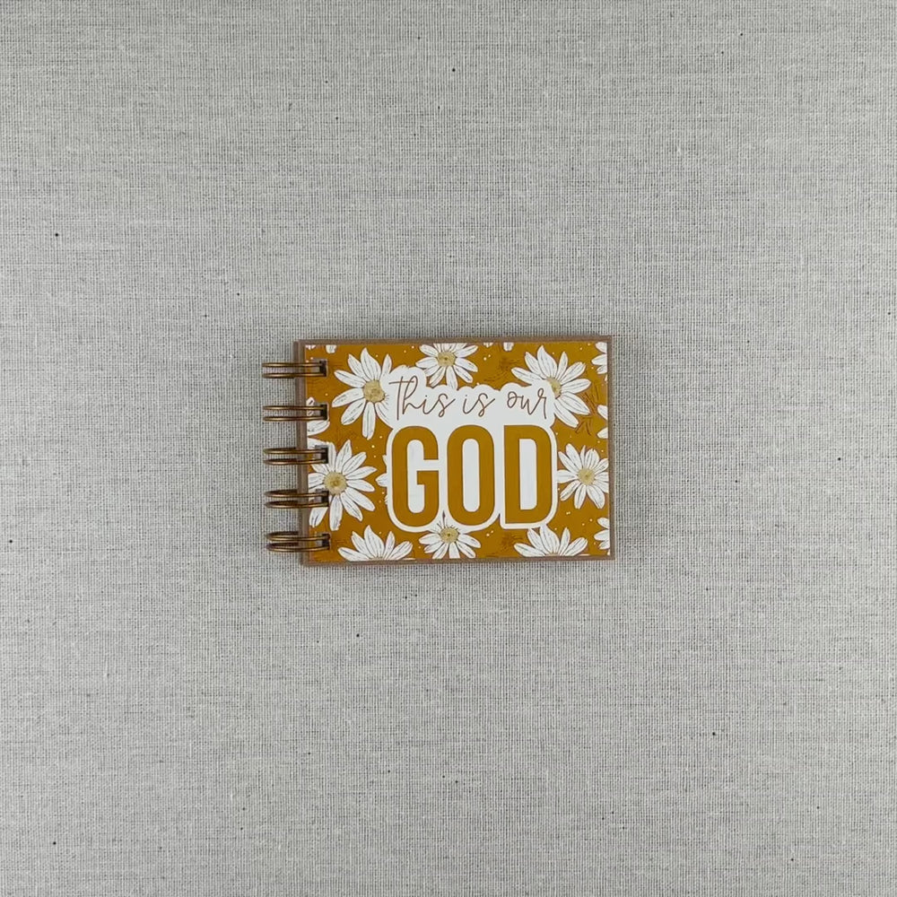 Video of small spiral bound attributes of God book in Daisy style with yellow background and ivory flowers. Front cover says "this is our GOD".