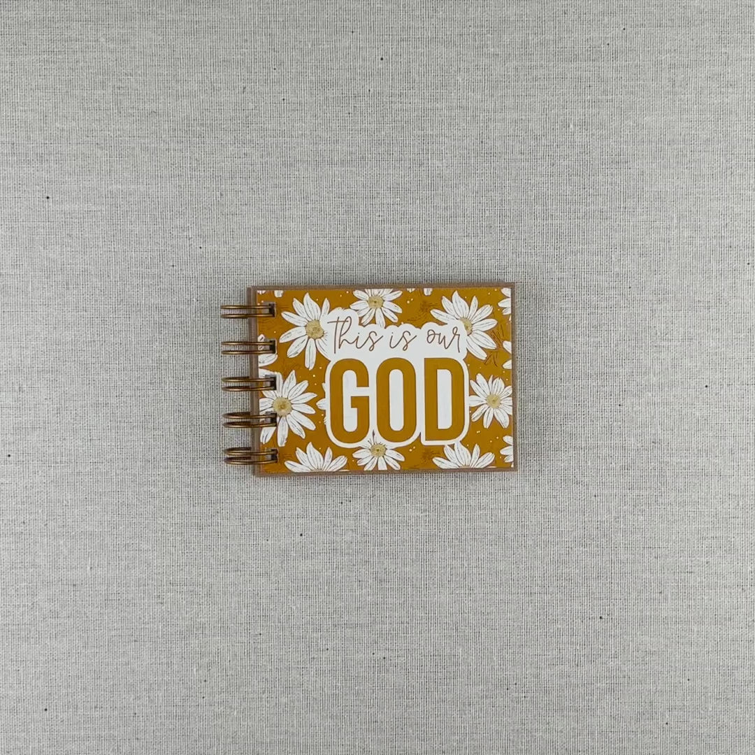 Video of small spiral bound attributes of God book in Daisy style with yellow background and ivory flowers. Front cover says "this is our GOD".