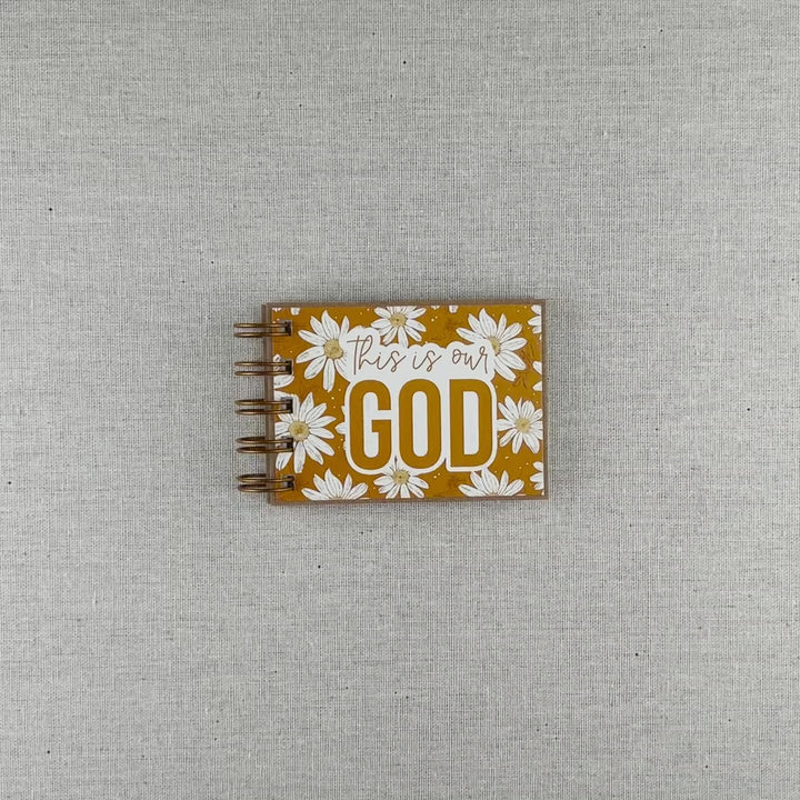 Video of small spiral bound attributes of God book in Daisy style with yellow background and ivory flowers. Front cover says "this is our GOD".