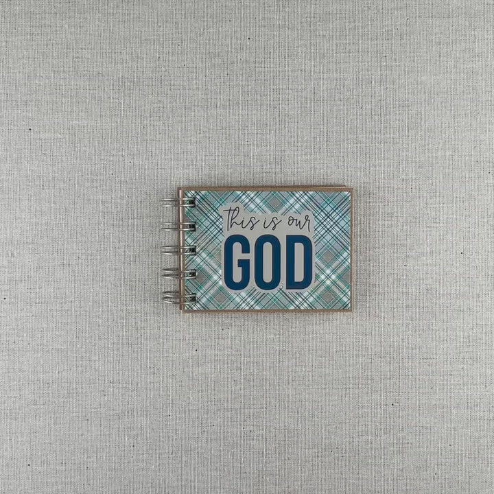 Video of spiral-bound book with 'This is our God' text on a plaid blue and gray cover.