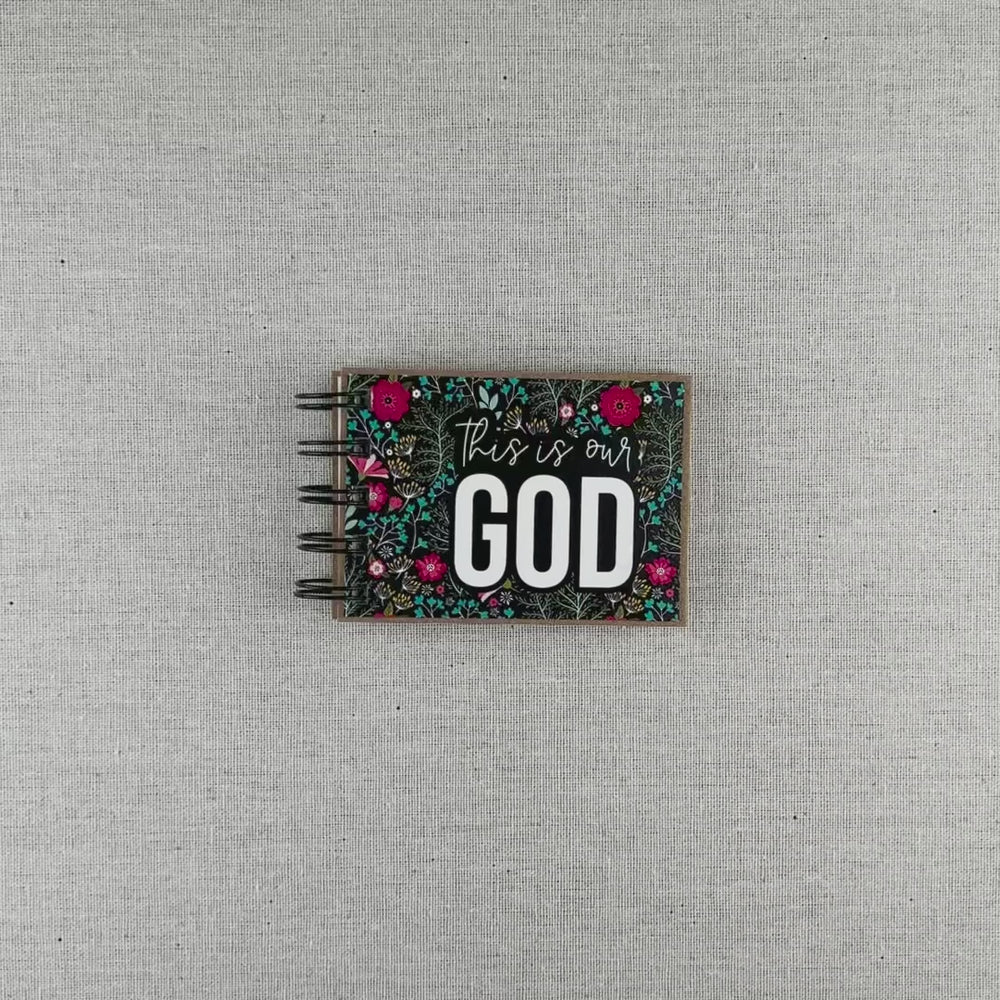 Video of God's attribute book with a black background and bright florals. The cover of this small, spiral-bound book says "this is our GOD".