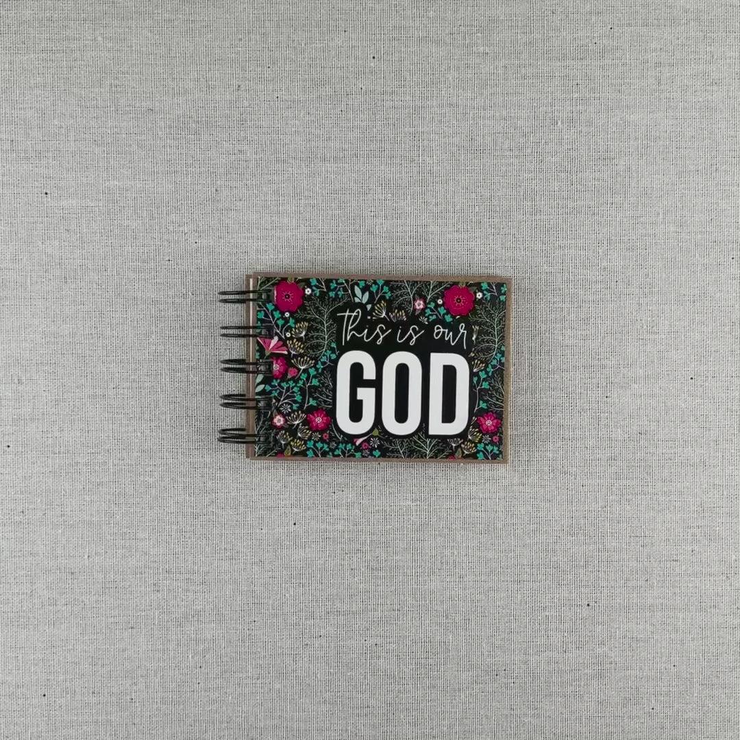 Video of God's attribute book with a black background and bright florals. The cover of this small, spiral-bound book says "this is our GOD".