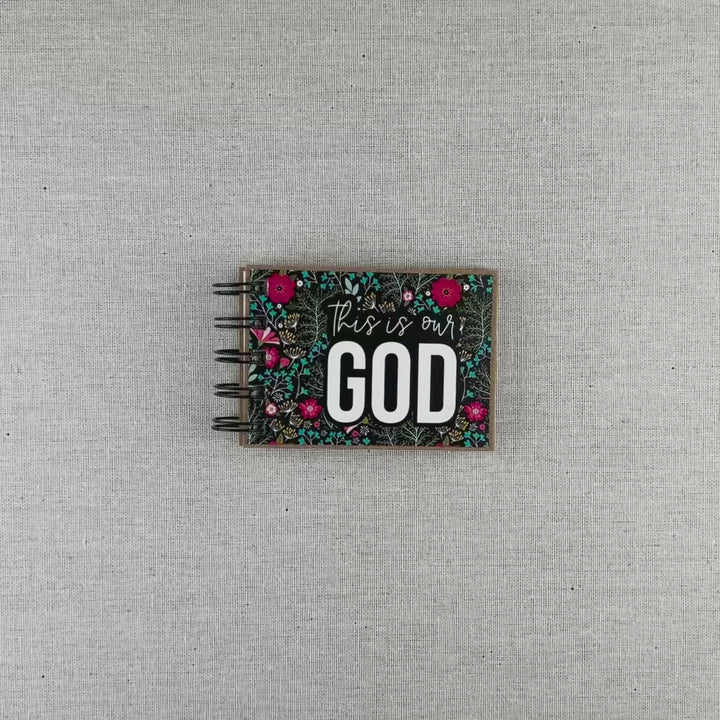 Video of God's attribute book with a black background and bright florals. The cover of this small, spiral-bound book says "this is our GOD".