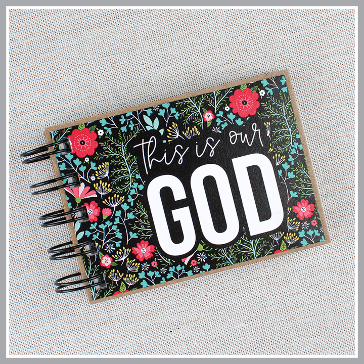 Front cover close up of God's attribute book with a black background and bright florals. The cover of this small, spiral-bound book says "this is our GOD".