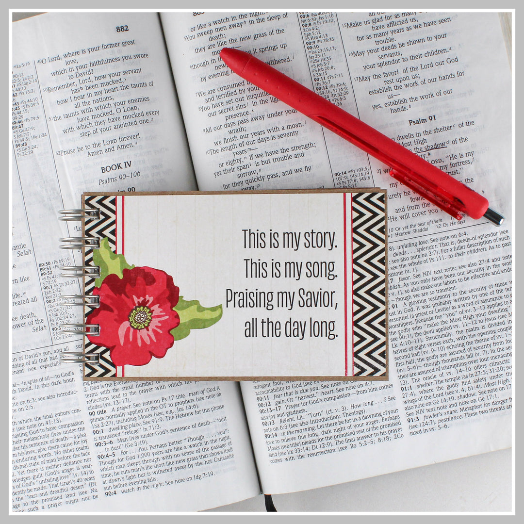 Red flower Christian journal resting on an open Bible for prayer, gratitude and daily quiet time.