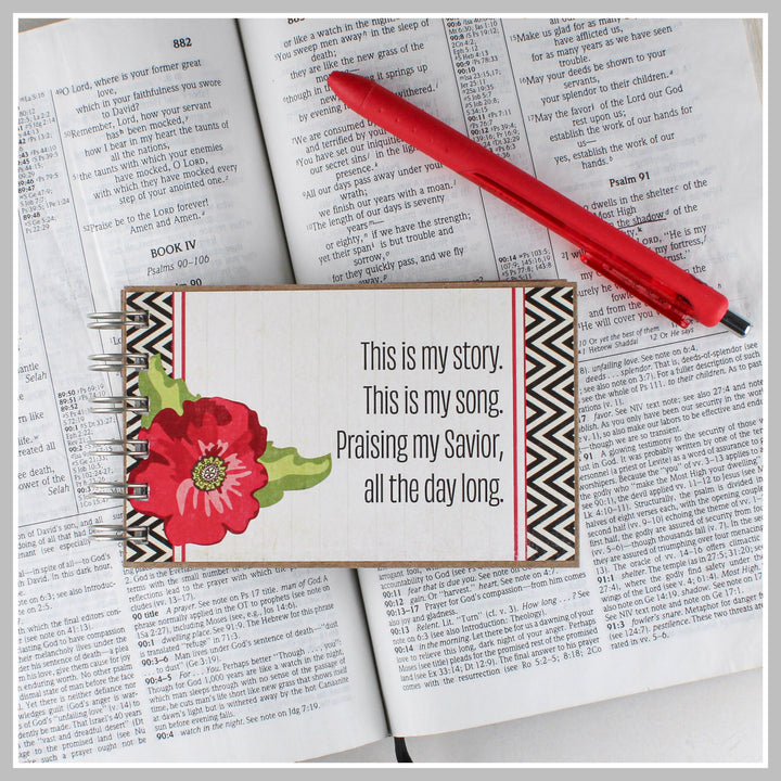 Red flower Christian journal resting on an open Bible for prayer, gratitude and daily quiet time.