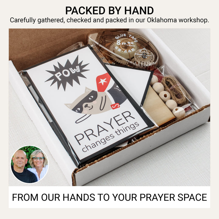Superhero prayer board kit packed by hand in an Oklahoma workshop, with matted graphics, wooden banner pieces, beads, twine, and adhesive.