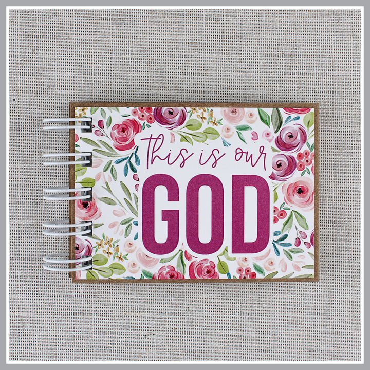 Close up of front cover of God's attributes book, spiral bound in Pastel Floral style with pink and purple floral background. Front cover says "this is our GOD".