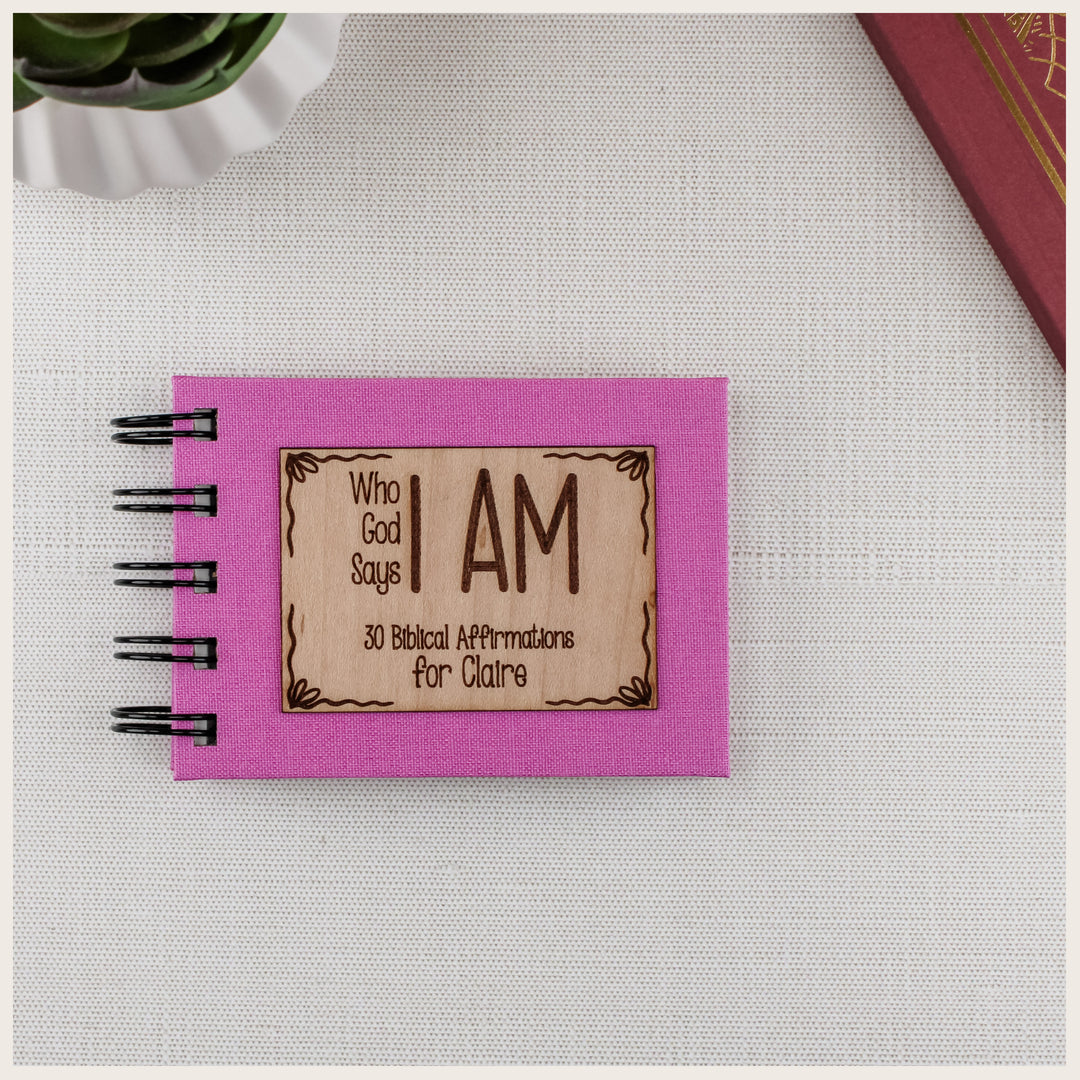 Pink Who God Says I AM spiral book with a bows wood plaque personalized for Claire and containing 30 biblical affirmations.