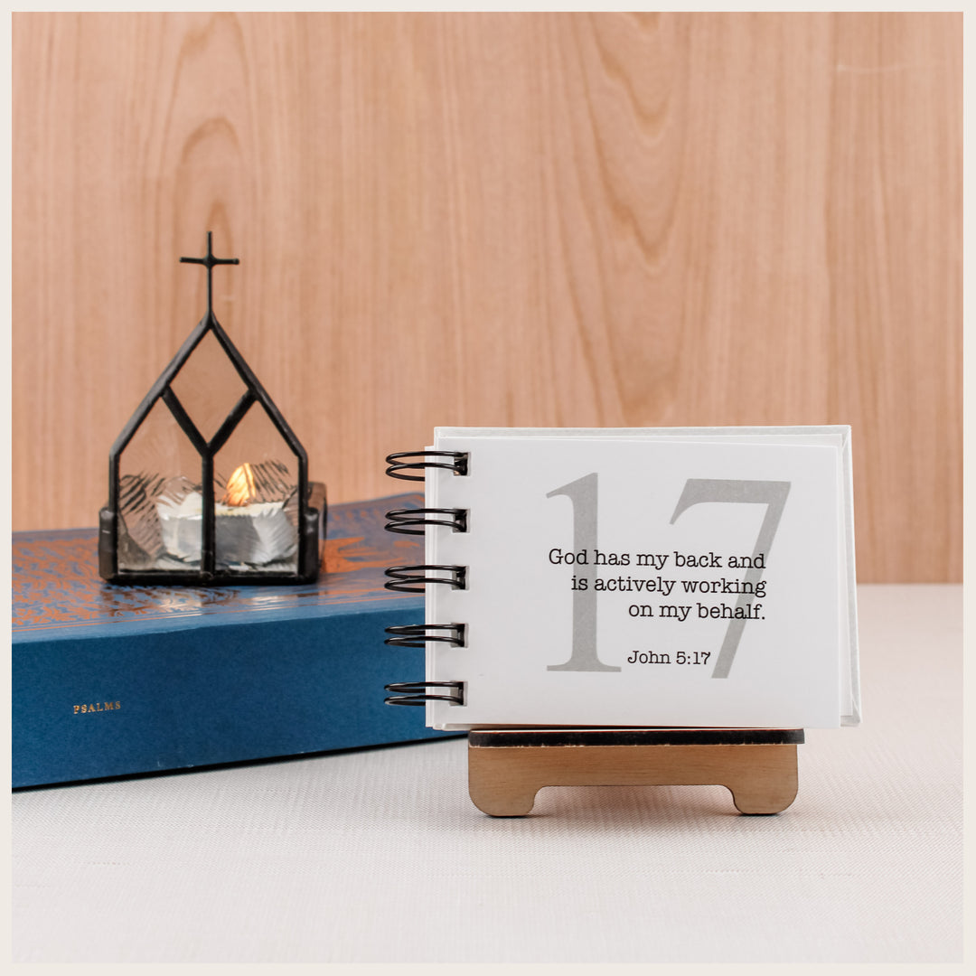 Wood easel holding an open affirmation book beside a blue Psalms book and church-shaped candleholder.